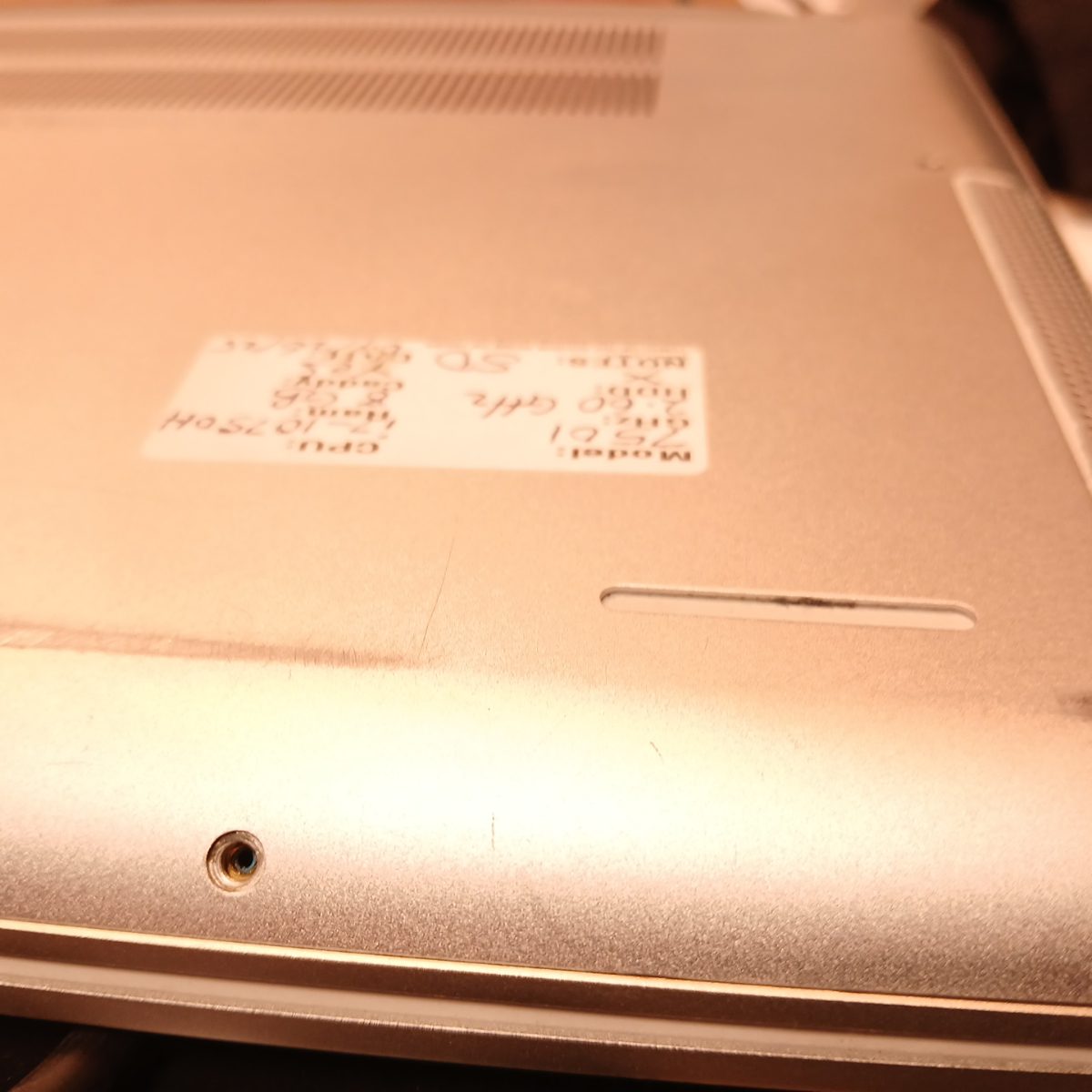 Bottom angled view of Dell Inspiron 15 7501 showing wear, feet, and handwritten inventory label